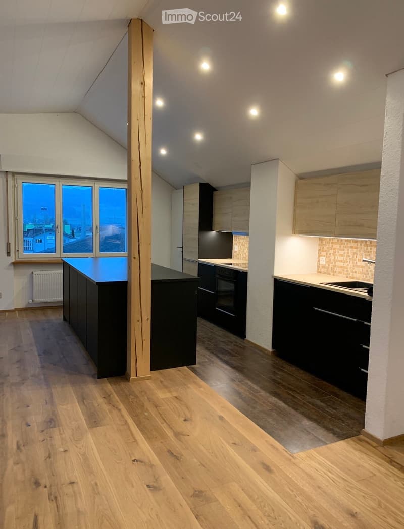 Modern kitchen with wooden flooring, black and light wood cabinets, a central island, and large windows overlooking a cityscape.