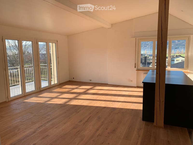 Bright, empty room with wooden flooring, large windows, and sliding glass doors leading to a balcony.