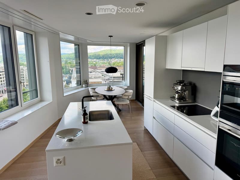 Modern kitchen with white cabinets, a central island, and a dining area. Features include a sink, coffee maker, oven, and a round dining table with chairs.