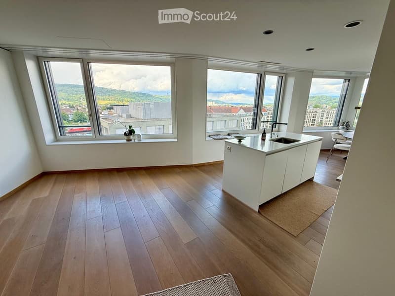 Modern kitchen with white cabinets, wooden flooring, large windows offering a scenic view, and a small seating area with a table and chairs.