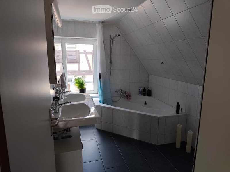 Modern bathroom with a double sink, bathtub, and large window with a view. Includes a plant on the windowsill and candles on the floor.