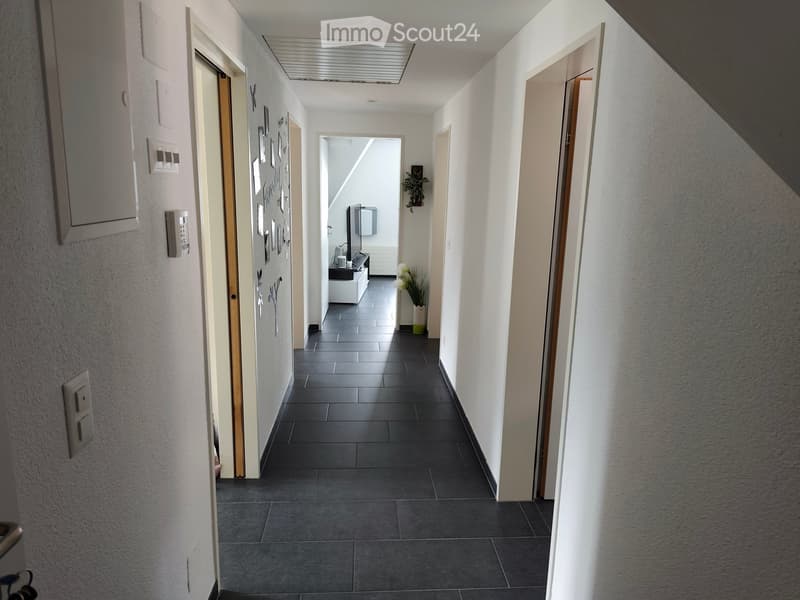 A modern hallway with dark tiled flooring, white walls, and several doors leading to different rooms. There are small decorative items and a plant visible in the background.