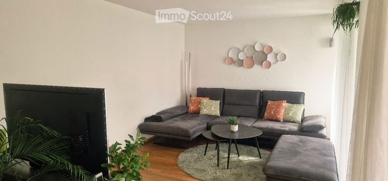 Modern living room with grey sectional sofa, colorful throw pillows, coffee table, ottoman, and wall art.