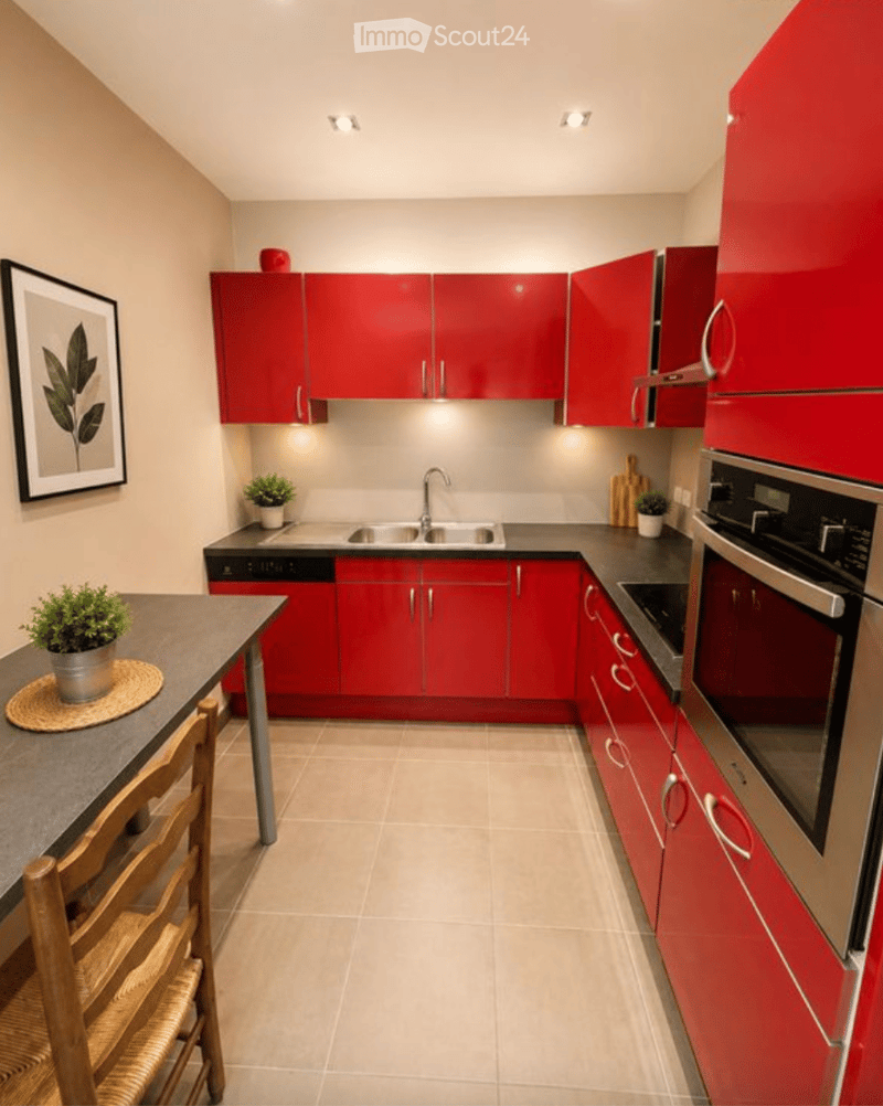 Modern kitchen with red cabinets, stainless steel appliances, and a small dining area with a table and chairs.