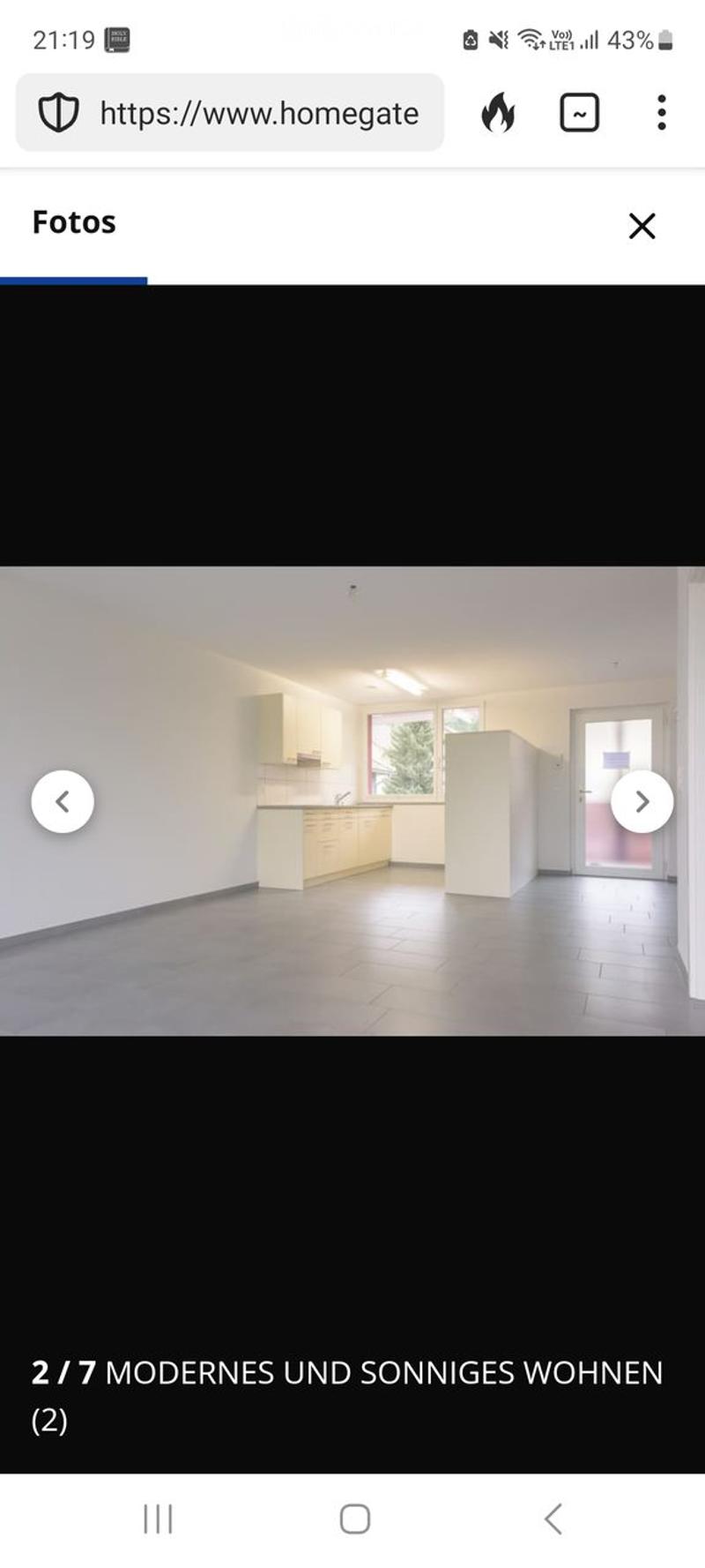 Empty kitchen with white cabinets, tiled floor, and large windows. No furniture or appliances are present.