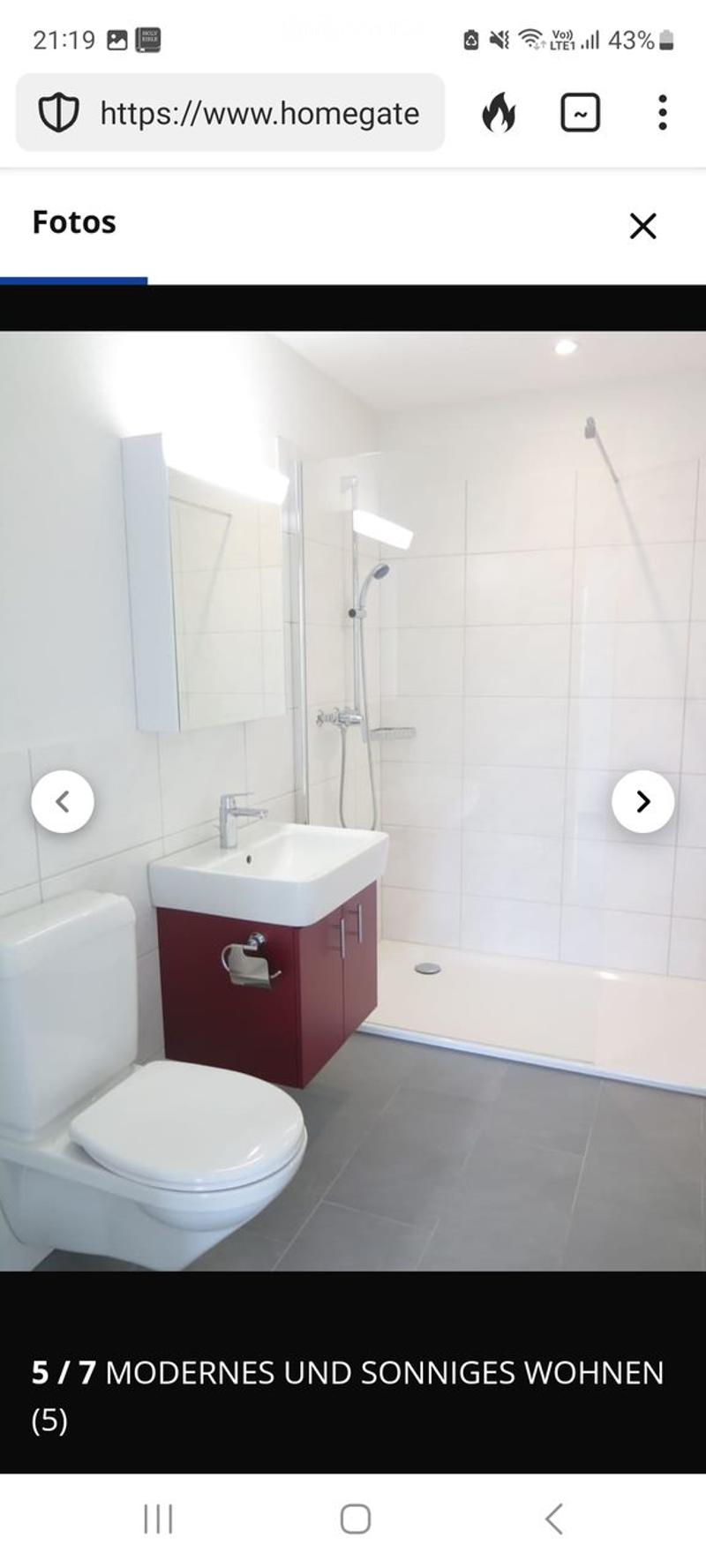 Modern bathroom with white tiles, a toilet, a sink with a red cabinet, a mirror, and a shower area.