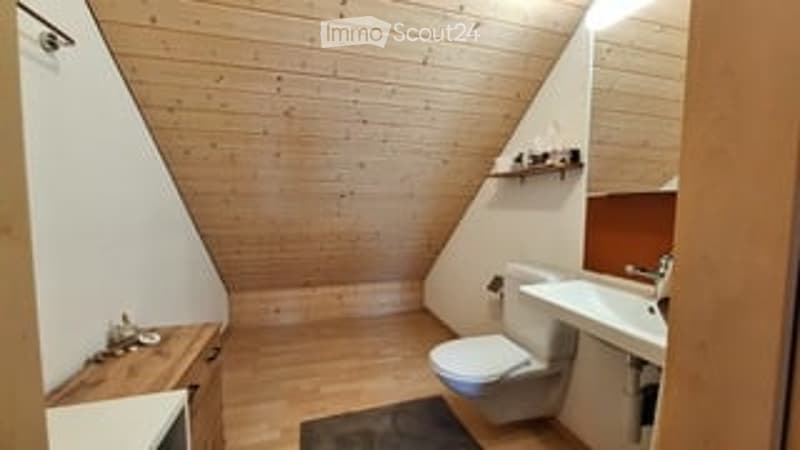 Cozy bathroom with wooden walls and floor, toilet, sink, and a small wooden shelf above the sink.