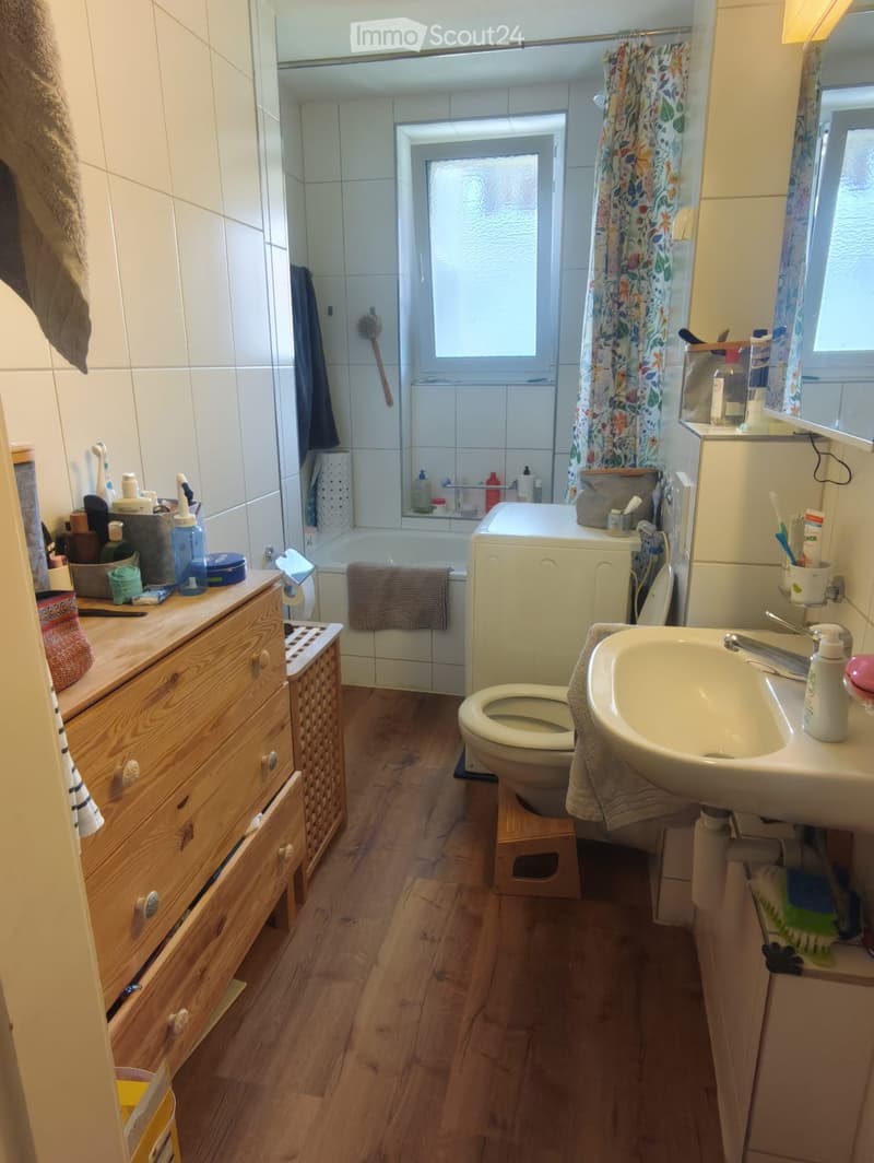 Bathroom with wooden floor, sink, toilet, bathtub, cabinet, and various toiletries.