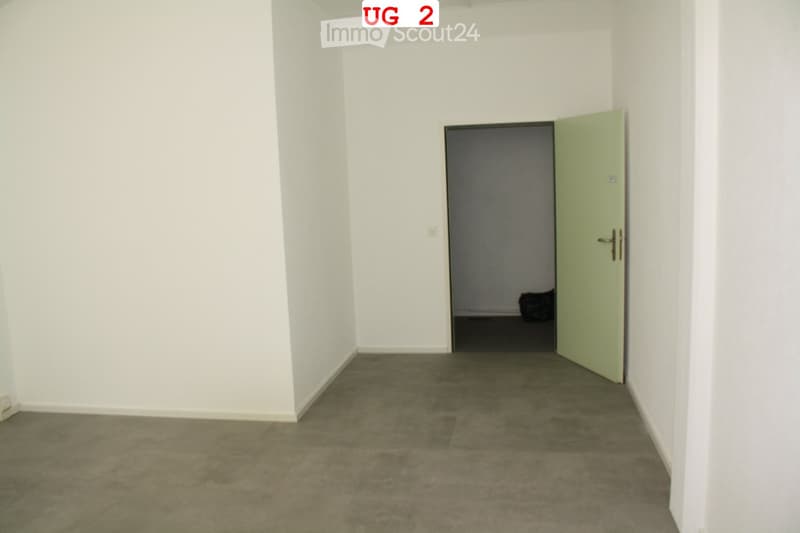 Empty room with white walls and a concrete floor, featuring an open doorway leading to another space.