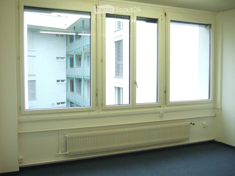 Empty room with large windows, radiator, and blue carpeted floor.