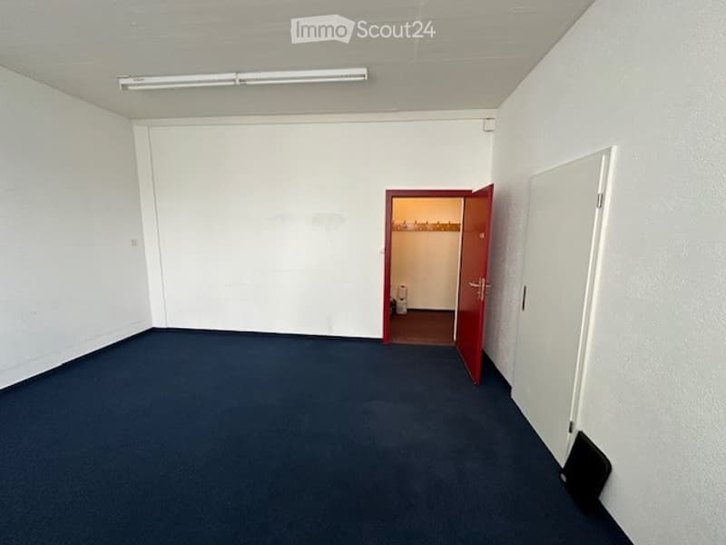 room with blue carpet, white walls, an entrance door, an open door leading to an empty room with a closet and a toilet