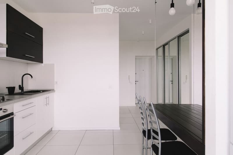 Modern kitchen with white cabinets, stainless steel sink, oven, and a dining area with a table and chairs.