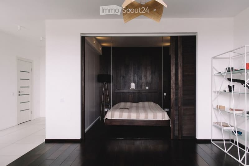 Modern bedroom with dark wooden walls, a bed with striped bedding, a white shelving unit, and a geometric wooden pendant light.