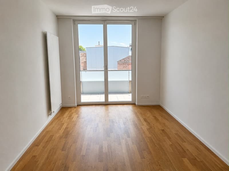 Empty room with wooden flooring, white walls, and large sliding glass doors leading to a balcony.