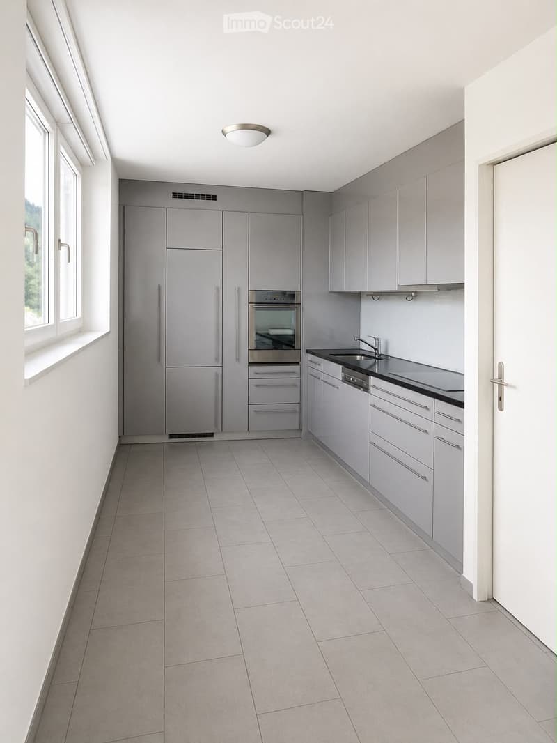 Modern kitchen with grey cabinets, stainless steel appliances, tiled floor, and large windows.