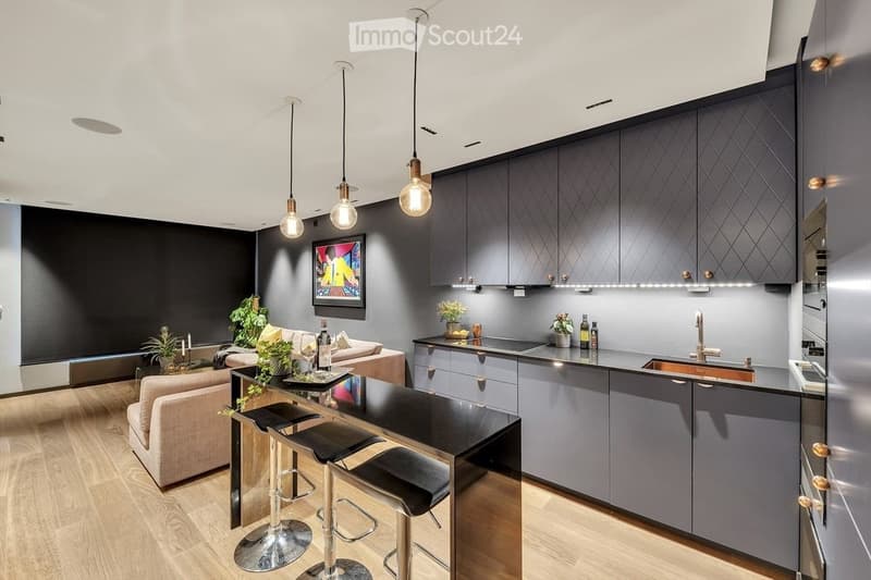 Modern kitchen and living area with grey cabinets, pendant lights, a sofa, coffee table, and bar stools.