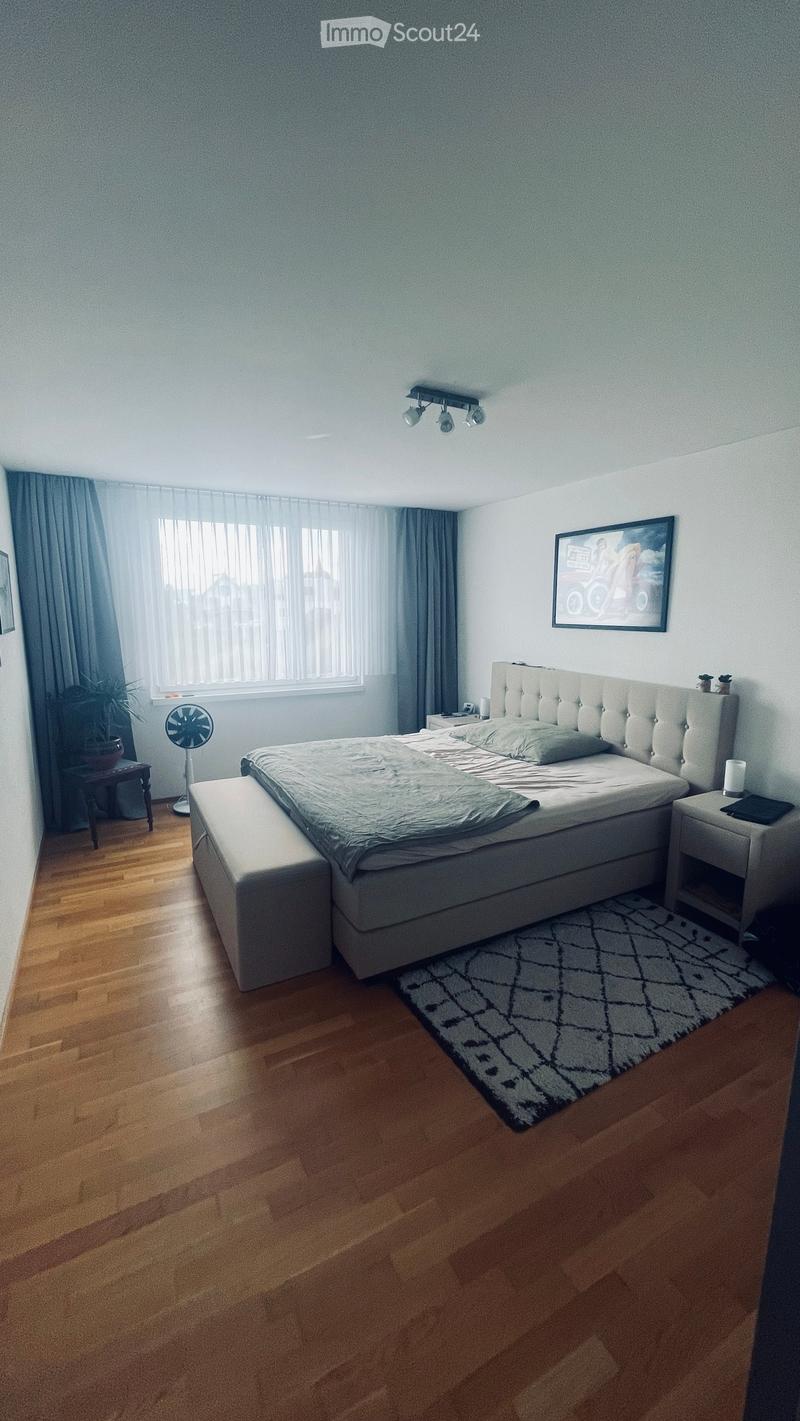 Modern bedroom with a large bed, nightstands, a fan, a small table with a chair, and a picture frame on the wall.