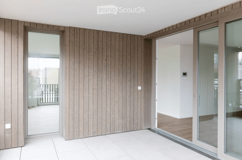 Empty room with wooden panel walls, white tiled floor, large glass doors leading to a balcony area.