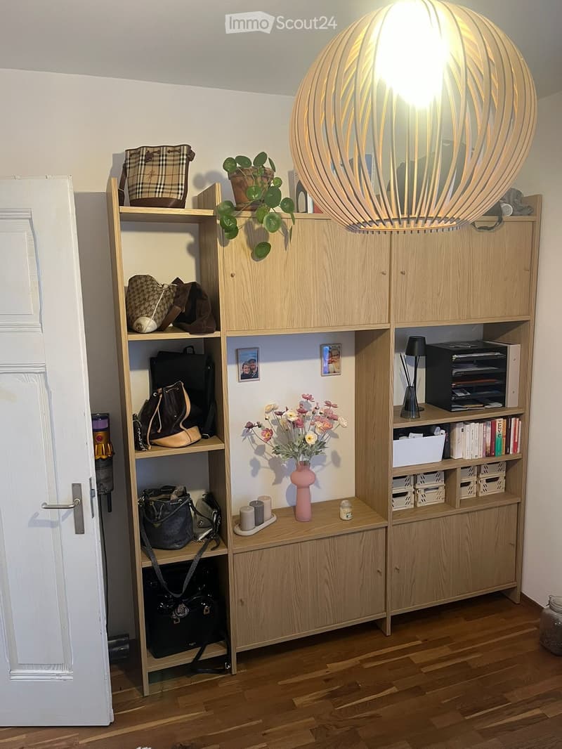 A well-organized entryway or hallway with wooden shelves and cabinets, featuring handbags, books, a vase with flowers, candles, and a decorative ball lamp.