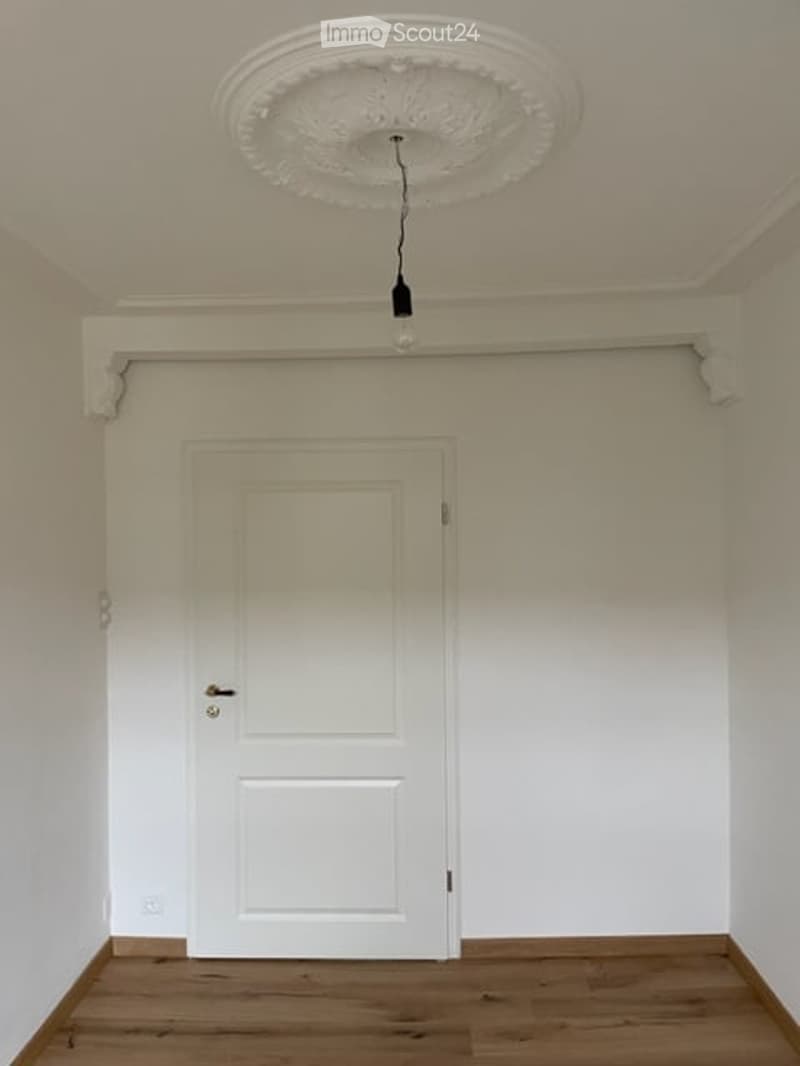 Empty room with white walls, wooden floor, white door, and a decorative ceiling light fixture.