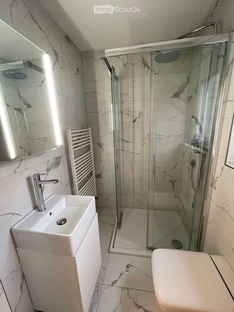 Modern bathroom with marble tiles, a white sink with a chrome faucet, a large mirror, a glass-enclosed shower, and a bathtub.