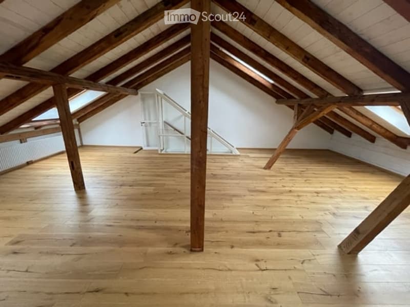 Empty attic space with wooden beams and polished wooden floor, featuring exposed wooden beams and a small staircase leading up.