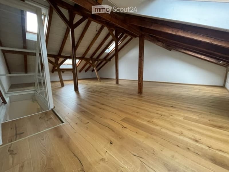 Empty attic space with wooden beams and exposed wooden floor, featuring skylights and a glass door leading to a balcony.