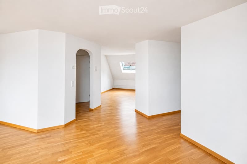 Empty room with light wooden flooring and white walls, featuring an arched doorway and a small window in the adjacent space.