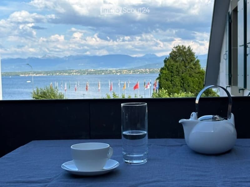 Balcony with a scenic view of a lake and mountains, featuring a small table with a cup, teapot, and glass.