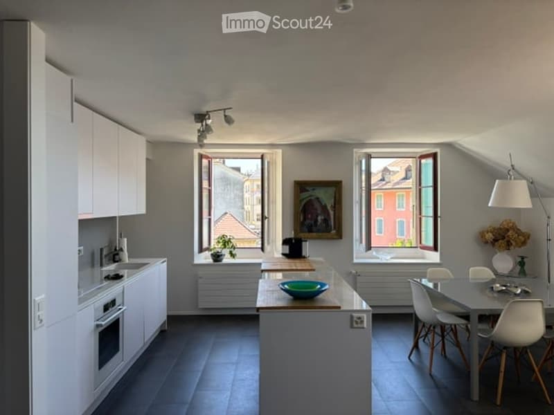 Modern kitchen with white cabinets, central island, dining area, and large windows offering a city view.