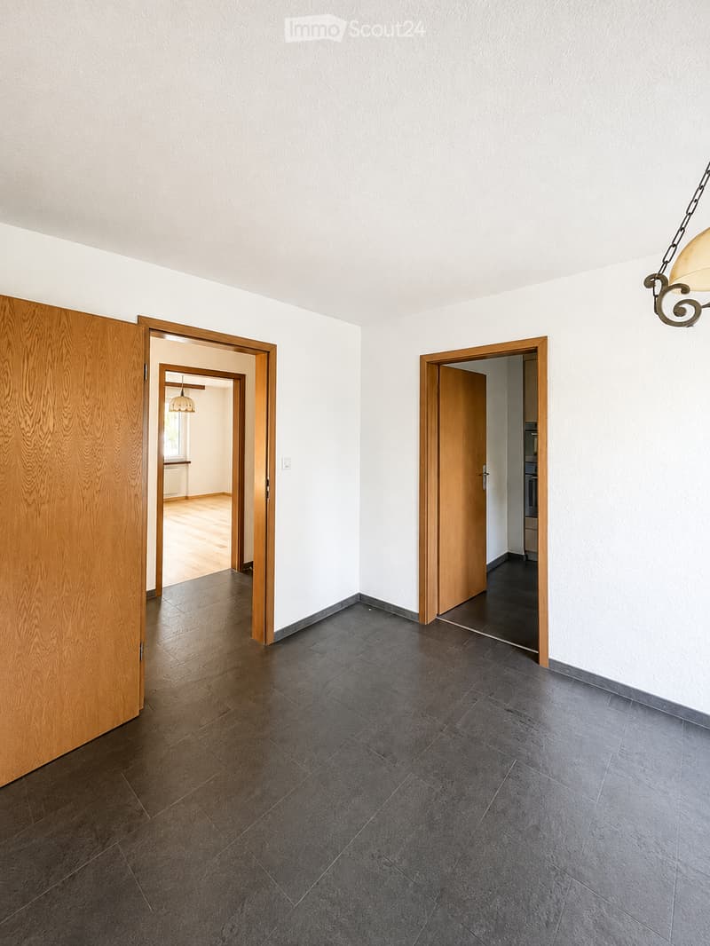 Empty hallway with dark tiled floor, white walls, and wooden doors leading to other rooms.