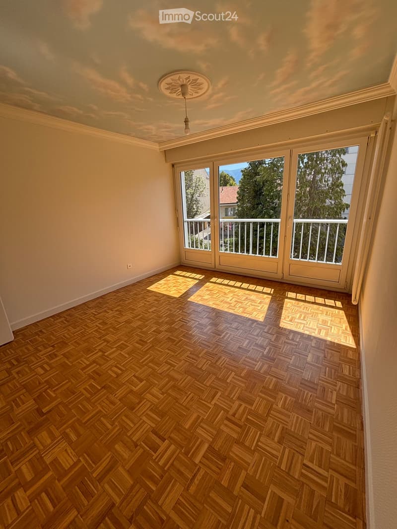 Empty room with wooden herringbone flooring, large sliding glass doors leading to a balcony, and a decorative ceiling light fixture.