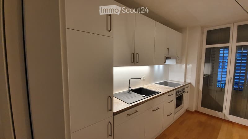 Modern kitchen with white cabinets, a sink, and an oven, featuring a wooden floor and a window with blinds.