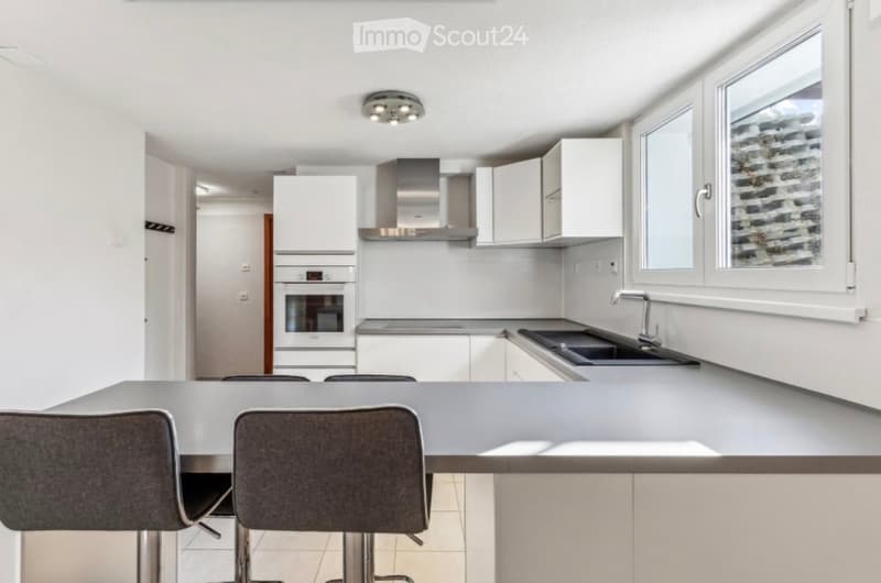 Modern kitchen with white cabinets, stainless steel appliances, a central island with bar stools, and large windows.