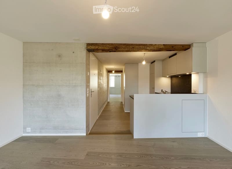Empty hallway with wooden flooring, white walls, and a small kitchen area visible at the end. No furniture or equipment present.