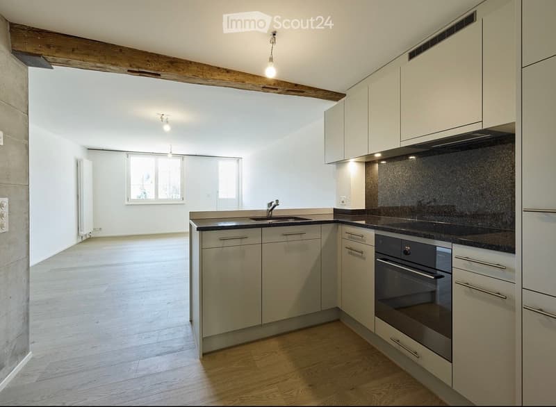 Modern kitchen with white cabinets, stainless steel sink, and oven. Light wooden flooring and exposed wooden beams on the ceiling.