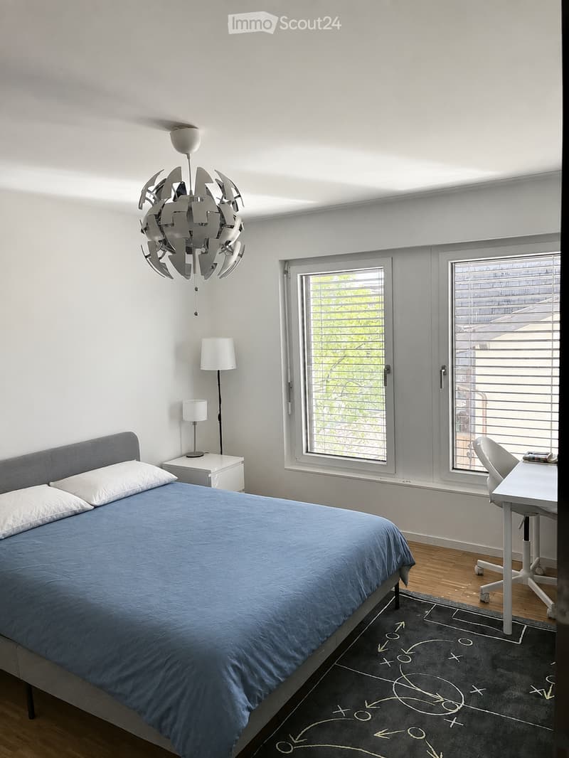 Modern bedroom with a blue bed, white pillows, nightstand, desk, chair, and a unique chandelier.