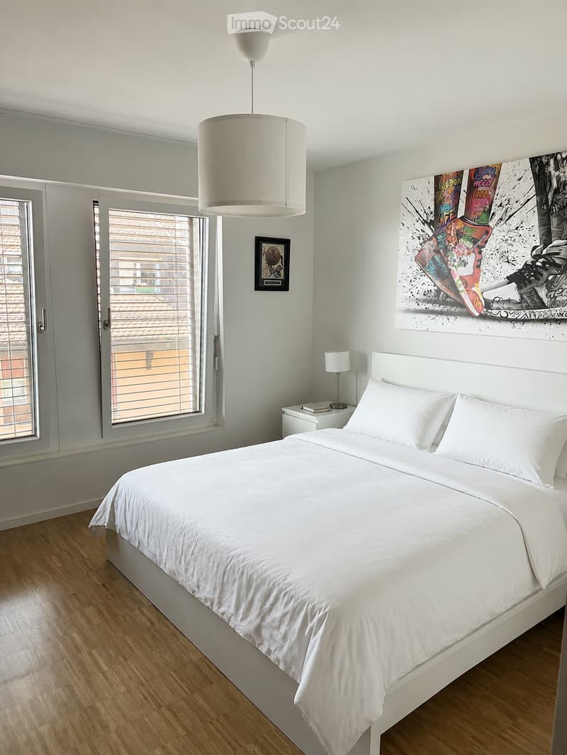 Modern bedroom with a white bed, nightstand, pendant light, and artwork on the wall.
