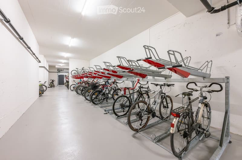 Clean, organized indoor bicycle storage area with multiple bicycles parked on racks against white walls.