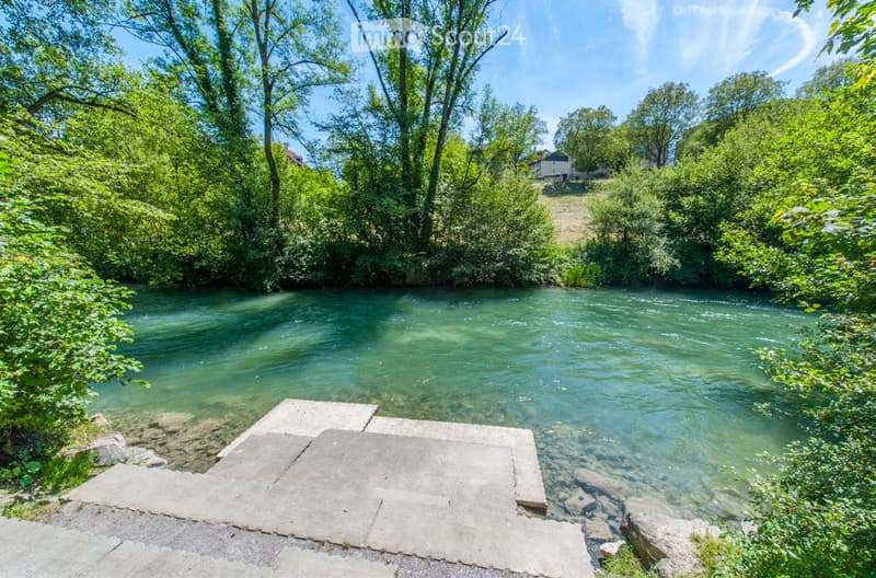A serene outdoor area featuring a clear river flowing through a lush, green landscape with trees and vegetation on both banks.