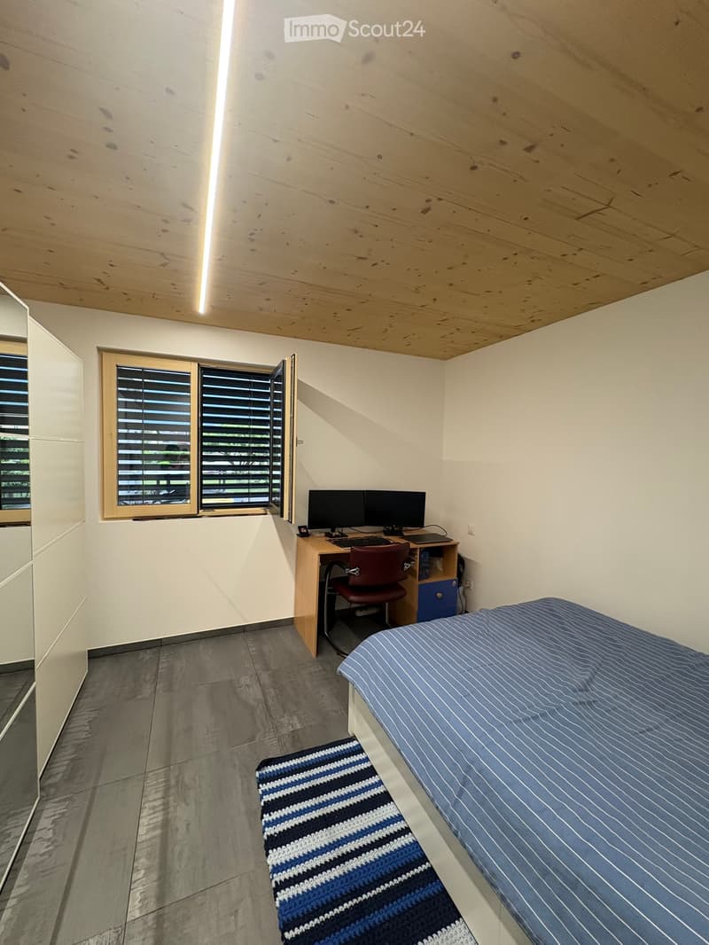Modern, minimalist bedroom with a single bed, desk with computer, chair, and a small rug.