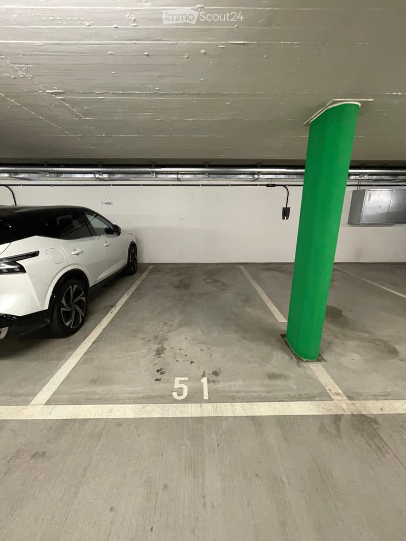 Underground parking space with a white car parked in bay number 51, marked with white lines and a green support pillar.