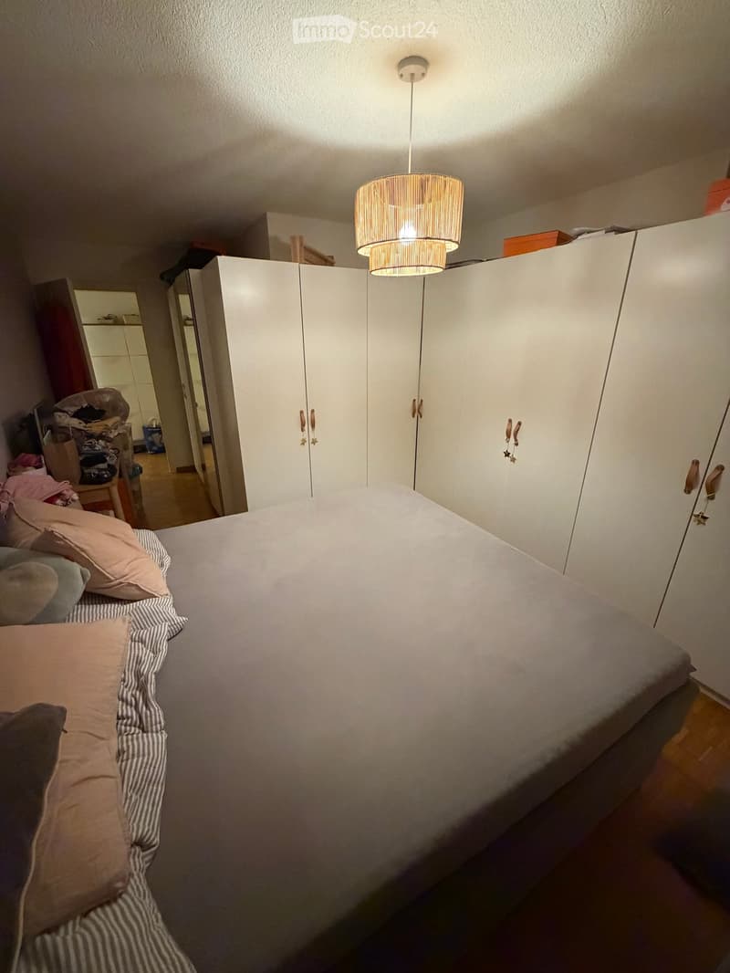 A tidy bedroom with a neatly made bed, pillows, a wardrobe, and a hanging lamp.