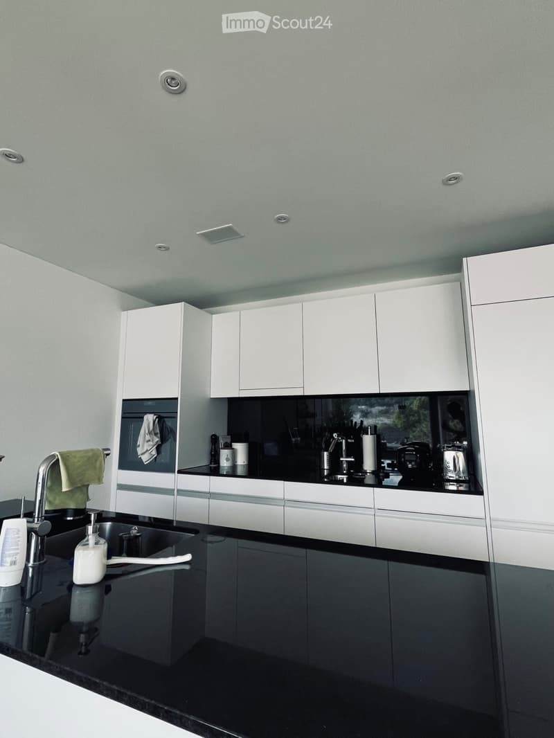 Modern kitchen with white cabinets, black countertops, stainless steel sink, and various appliances including a coffee maker and oven.