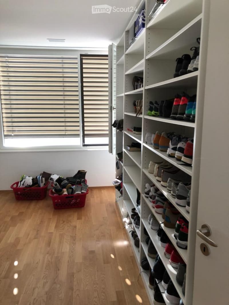A well-lit, organized closet with wooden flooring, white walls, and built-in shelving units filled with shoes and storage baskets.