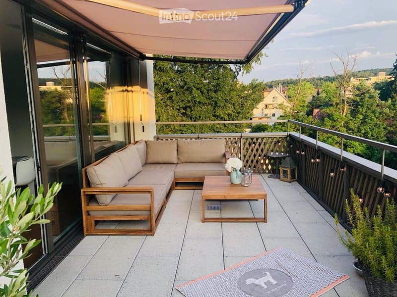 Balcony with a sectional sofa, coffee table, and decorative items, overlooking a green landscape.