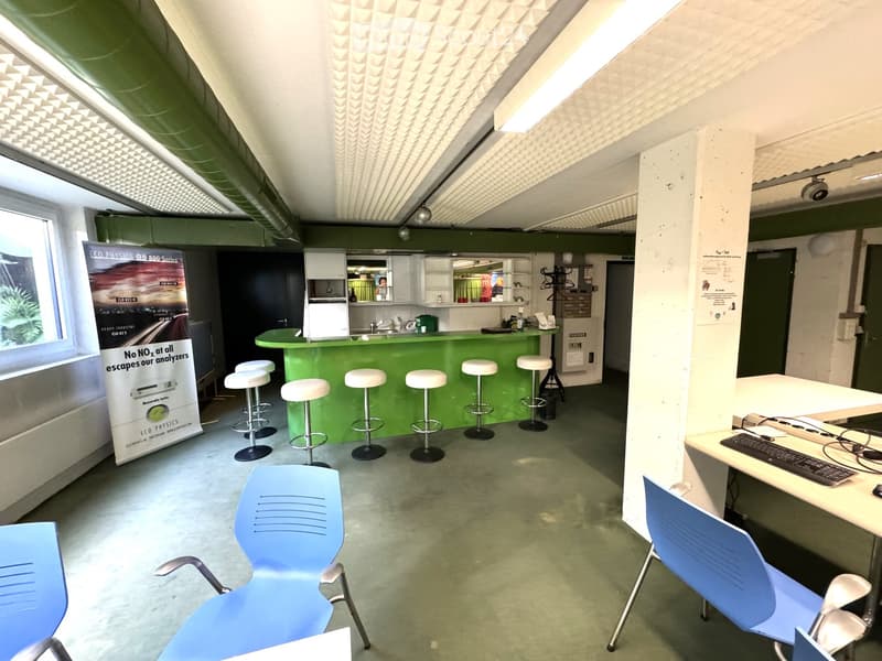 A room with a green counter, stools, blue chairs, a desk with a computer, a banner, and a window.