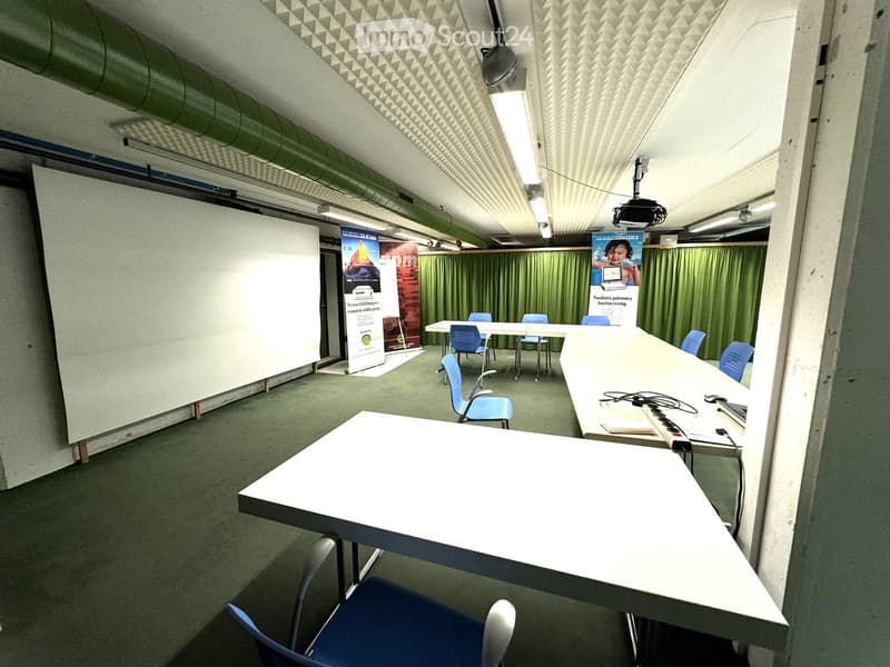 Empty room with white walls, green carpet, long white tables, blue chairs, whiteboard, green curtains, posters, projector