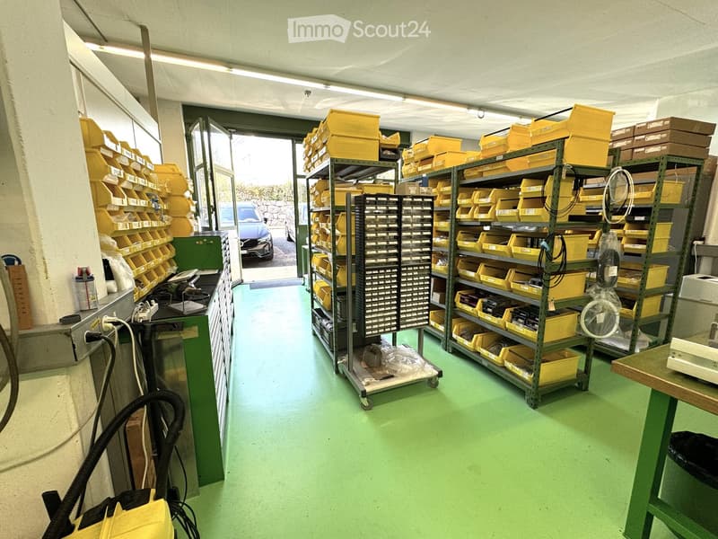 Warehouse with green floor, yellow storage boxes, shelves, trolleys, electrical outlets, and a car parked outside