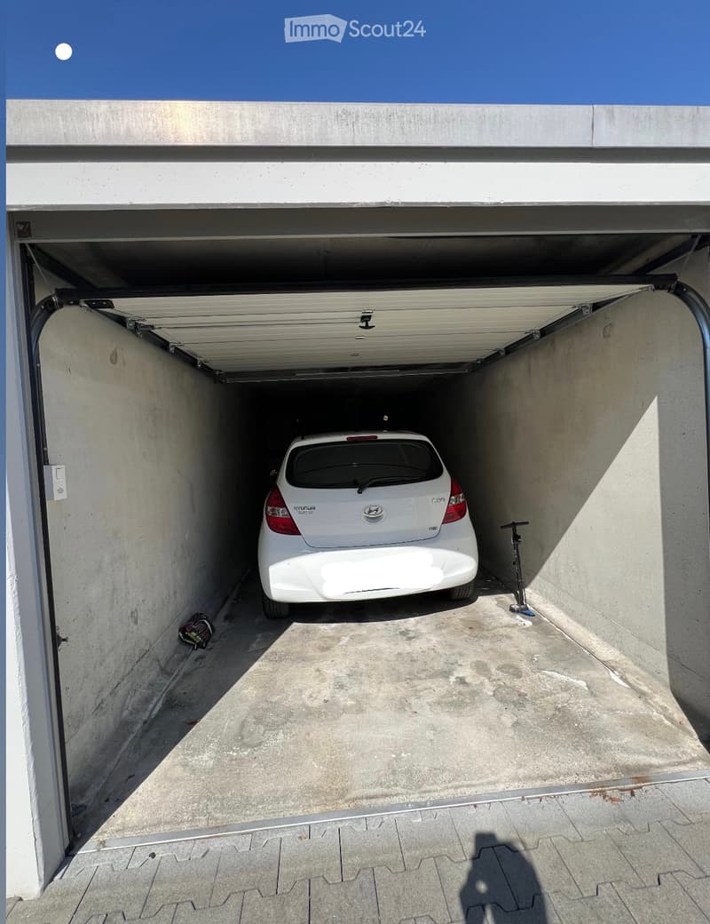 Underground parking space with a white car parked inside, concrete walls, and a raised ceiling.